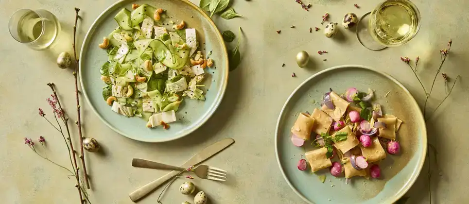 Laat je inspireren door ons biologische weekmenu vol frisse lentegerechten Twee borden met frisse biologische lentegerechten uit het Ekoplaza weekmenu: een groene salade met komkommer en cashewnoten, en een pastagerecht met radijsjes.