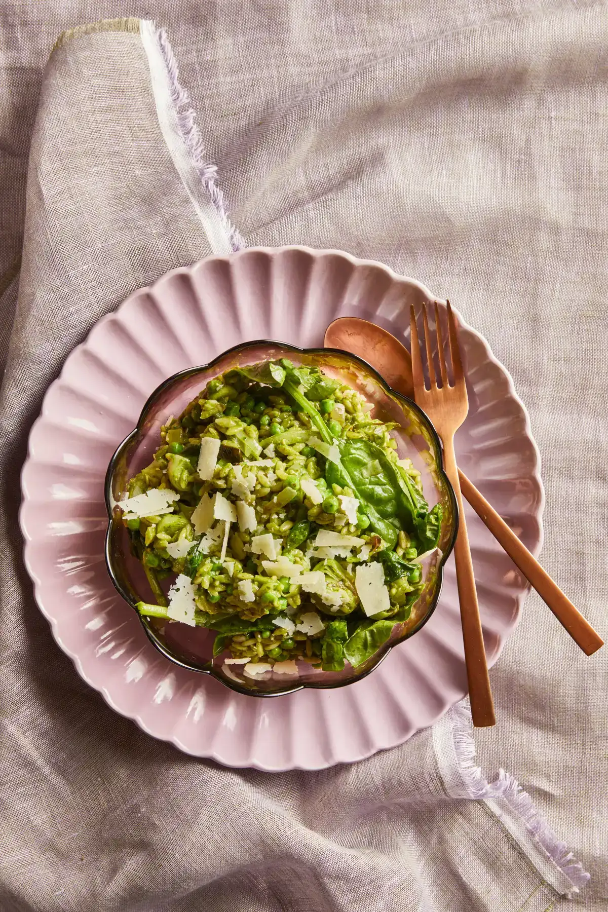 Een bord met romige orzo met doperwten, spinazie en prei van Ekoplaza op een roze ondergrond