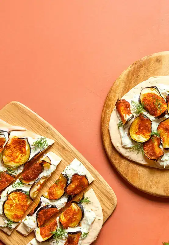Een houten serveerplank met flatbread, besmeerd met tzatziki en belegd met zoete aubergine